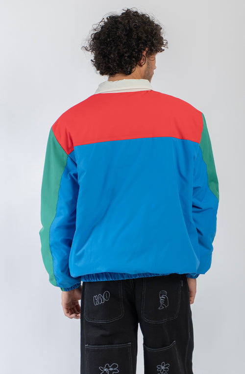 Chaqueta Kangaroo color block azul, verde, rojo y marfil con media cremallera y logo Kaotiko Society.