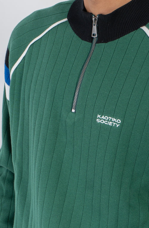 Jersey de punto verde con media cremallera, cuello alto y detalles deportivos en blanco, negro y azul.