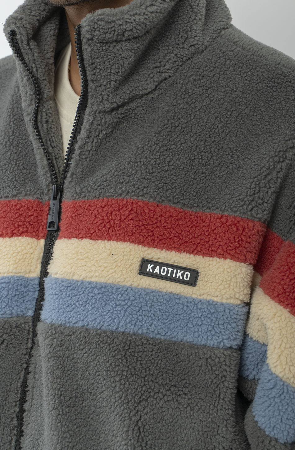 Polar Wabi Sabi Khaki de fleece con franjas rojas, beige y azules, cuello alto y cierre de cremallera.